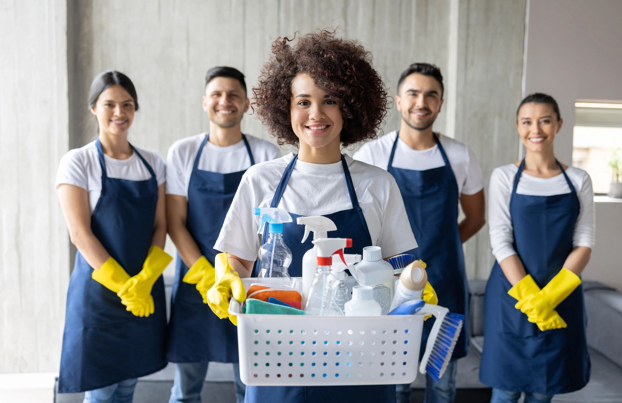 Cleaner holding a basket of cleaning supplies with team behind